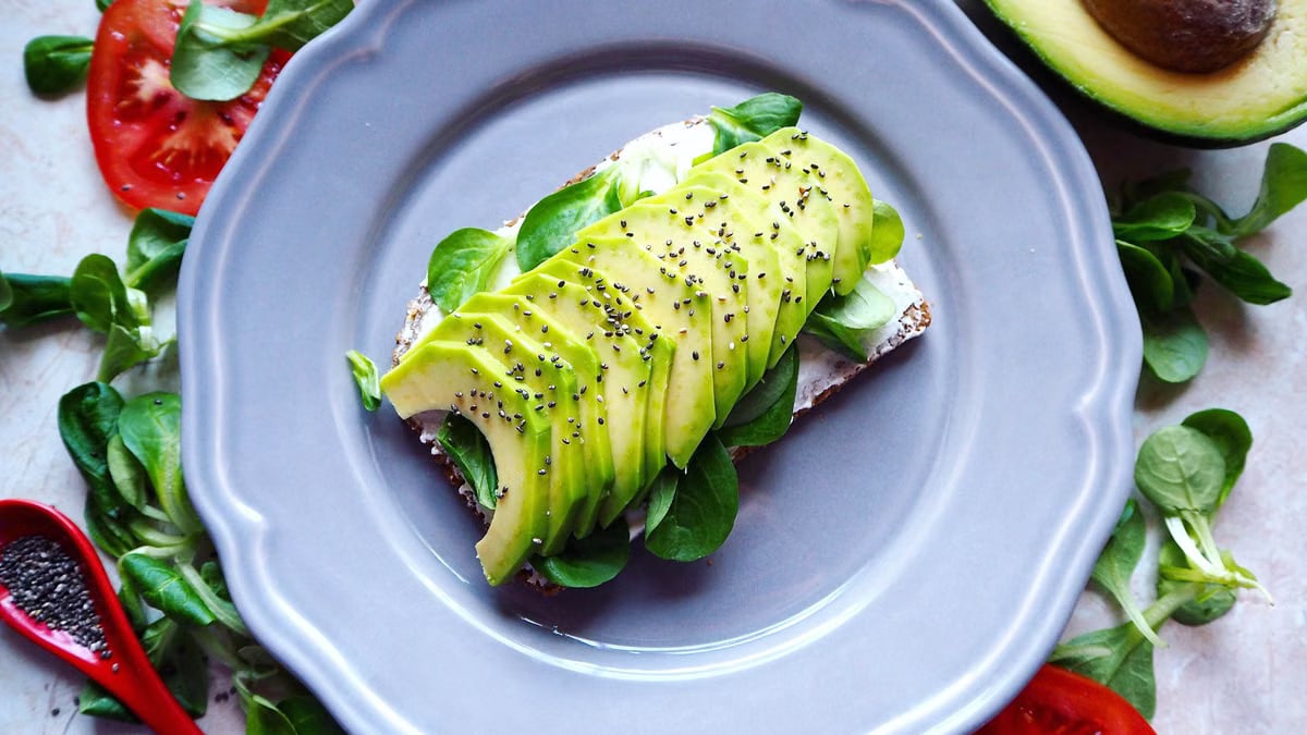 Delicious avocado toast with chia seeds and fresh tomatoes on a grey plate.