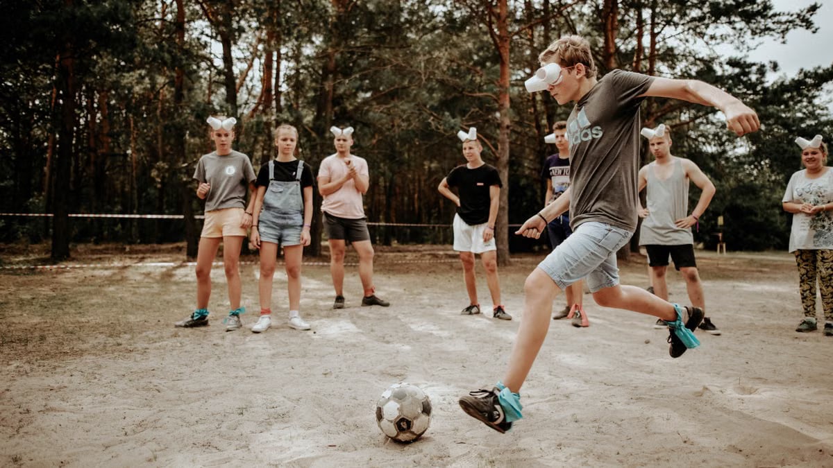Teenagers enjoying an outdoor soccer game with a humorous twist using eyecovers as a challenge.